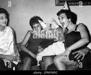 Circa 1960: adulti che festeggiano a casa con cappelli da festa, USA., originale fotografia vintage in bianco e nero. Foto Stock