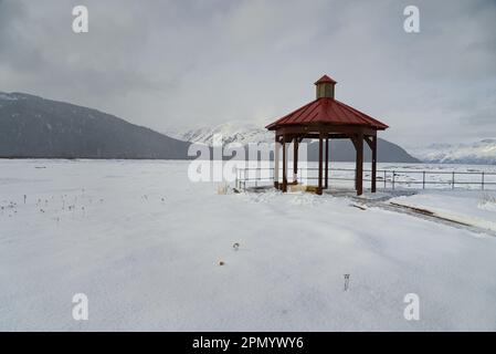 Gazebo rosso in campo innevato bianco in una giornata nuvolosa. Foto Stock