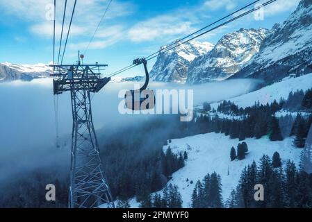 Cabinovia che si sposta sulla foresta tra le montagne innevate Foto Stock