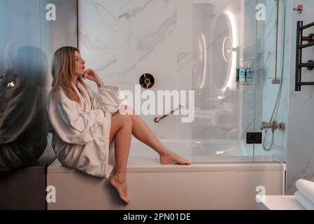 Una donna premurosa che si siede nella vasca da bagno nel bagno dell'hotel di lusso Foto Stock