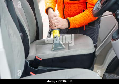 Sedile anteriore in tessuto per auto con aspirapolvere per uomo. uomo che pulisce la macchina da lavoro Foto Stock