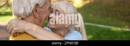 Donna matura sorridente con marito in abbraccio sportivo in verde parco Foto Stock