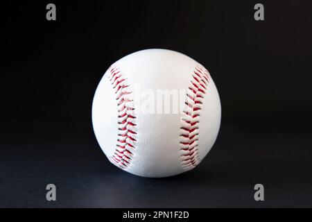Primo piano di un baseball bianco con cuciture rosse su sfondo nero Foto Stock