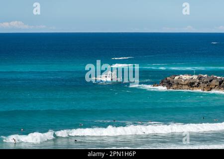 Vista della gente nel surf a Duran bar Beach, un peschereccio da traino che esce dalla foce del fiume Tweed, e la gente in moto d'acqua sul mare turchese. Foto Stock