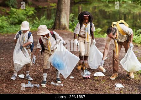 Un gruppo di scout lungo e diversificato che raccolgono rifiuti nella foresta durante un viaggio sul campo con consapevolezza ecologica Foto Stock