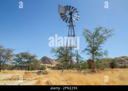 Una pompa a vento e un canale d'acqua in terreni agricoli al pascolo in Namibia. Foto Stock