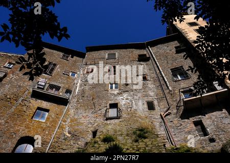 Vecchie case con lunghi tubi di scolo, finestre sostituite e pareti in pietra accanto alla torre della scala di Palazzo Orsini a Bomarzo, Lazio, Italia, convertite in grande palazzo rinascimentale dal 1500s capo militare pensionato Duca Vicino Orsini. Sotto di essa, ha creato la Villa delle meraviglie, con terrazze recanti bizzarre opere manieriste e oggi noto come Parco dei Mostri. Foto Stock