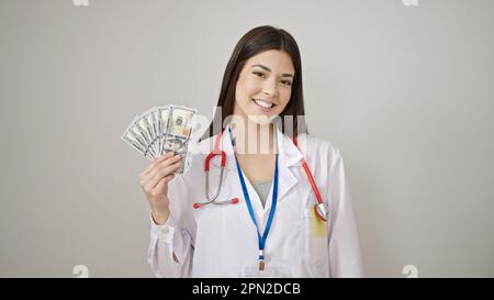 Giovane bella donna ispanica medico sorridente sicuro tenendo i dollari su sfondo bianco isolato Foto Stock