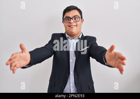 Giovane uomo ispanico con sindrome di Down indossare stile business guardando la fotocamera sorridente con le braccia aperte per abbracciare. espressione allegra che abbraccia humi Foto Stock