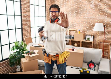 Bell'uomo di mezza età che tiene il cacciavite a casa nuova facendo smettere di cantare con il palmo della mano. espressione di avvertimento con gesto negativo e serio attivato Foto Stock