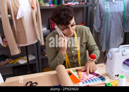 Non binary man Tailor Talking su smartphone cercando colore test presso atelier Foto Stock