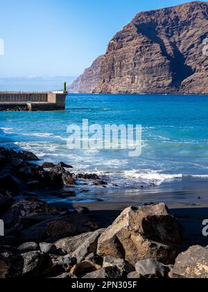 Luce del sole sulle maestose scogliere di Los Gigantes e la sabbia nera della spiaggia di Playa Los Guíos, con l'ingresso al porto di Los Gigantes e rocce aspre. Foto Stock
