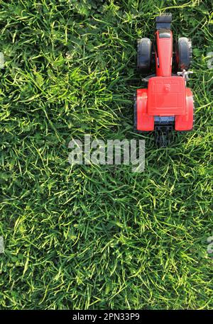 Lavori agricoli primaverili. Modello di trattore rosso sull'erba verde. Piantando cereali. Trattore agricolo su sfondo verde. Vista dall'alto del trattore giocattolo Foto Stock