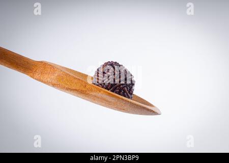 La caramella 'Brigadier' viene preparata in un cucchiaio di legno con diversi dolci 'brigadeiro' su una ciotola bianca con spruzzate di cioccolato giacenti sul tavolo. Laterale v Foto Stock