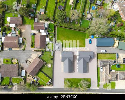 Vista aerea dall'alto verso il basso di una coppia di nuovi bungalow staccati visti adiacenti a case e giardini stabiliti. Foto Stock