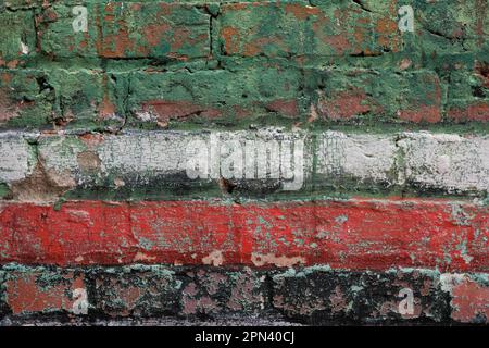 Parete in mattoni verniciata e intaccata con strisce rosse, verdi e nere. Foto Stock