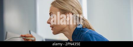 Nurse on Duty fa annuncio nel microfono seduto al banco di ricevimento nella clinica moderna Foto Stock