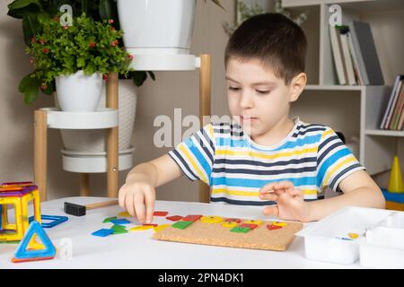 Un ragazzo di 5 anni crea un'immagine da pezzi multicolore di un mosaico su una lavagna. Foto Stock