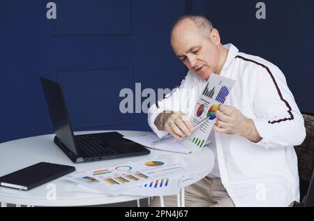 Un uomo effettua una videochiamata online, seduto a casa e parlando con una webcam del laptop, mostrando un documento. Foto Stock