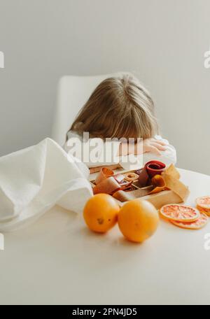 Una ragazza in un cappotto bianco si è addormentata o è triste seduta ad un tavolo su cui si erge un marshmallow di frutta. Foto Stock