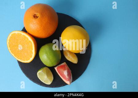 Agrumi, arancia, limone, pompelmo, lime giacciono su un vassoio nero su sfondo blu con spazio per testo e inventario. Frutti sani. Vitamina C. Foto Stock