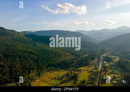 Vista aerea della serata nebbia sulle piccole case di un villaggio di montagna tra alte vette con alberi di pino scuro al tramonto luminoso. Amazingl scenario di Foto Stock