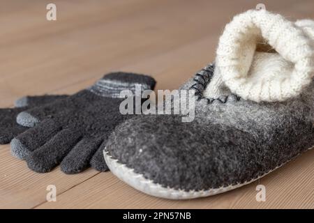 Sul pavimento in legno si trovano le pantofole da uomo in lana secca, un calzino in lana fatto a mano e guanti di colore naturale. Foto Stock