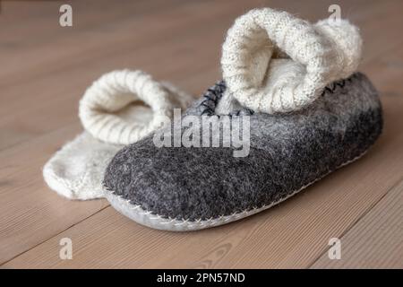 Sul pavimento in legno di casa ci sono pantofole da uomo in lana e calzini di lana lavorati a maglia Foto Stock