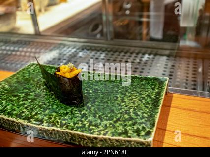 Rotolo di sushi caldo isolato su una piastra di ceramica verde Foto Stock