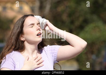 Donna stressata sudorazione ed essiccazione con un tessuto in un parco in estate Foto Stock