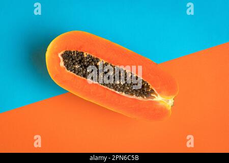 Papaya matura tagliata a metà su fondo blu e arancione. Concetto estivo. Foto Stock