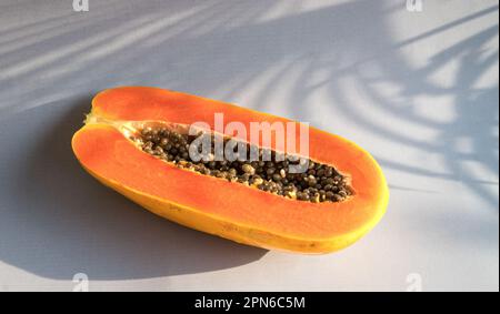 Papaya matura tagliata a metà su sfondo chiaro con foglie di palma d'ombra. Spazio di copia. Foto Stock