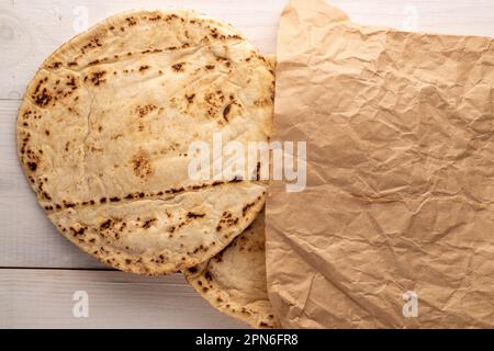 Due pita appena sfornata in un sacchetto di carta, primo piano, su un tavolo di legno, vista dall'alto. Foto Stock