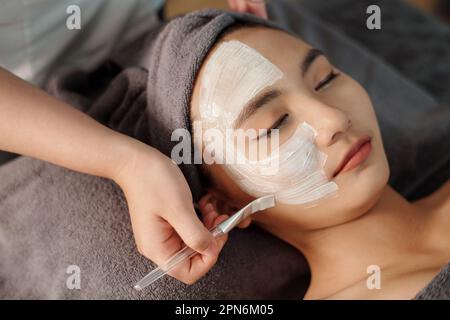 Estetista applicare maschera di argilla bianca sul viso della giovane donna Foto Stock