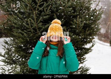 donna in cappello giallo, occhiali e giacca verde in caduta di neve in inverno Foto Stock