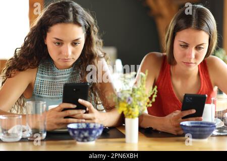 Vista frontale di due amici in un ristorante che si ignorano l'un l'altro utilizzando il telefono Foto Stock