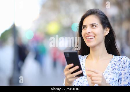 Donna felice che tiene il telefono delle cellule guarda in su nella strada Foto Stock