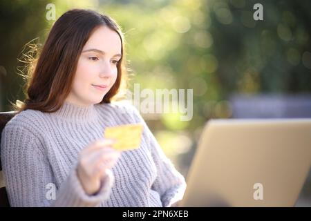 Donna seria che acquista con carta di credito e portatile sititng in un parco Foto Stock