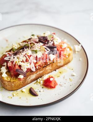 Dakos insalata tradizionale greca insalata con fette biscottate di orzo o pane ammollato e croccante, condita con pomodori succosi, formaggio feta, cipolle, olive, e un Foto Stock