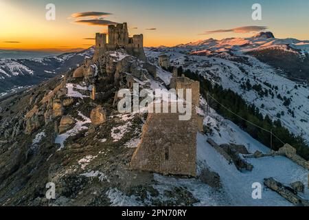 Veduta aerea della Rocca di Calascio con neve e illuminata dalla luce del tramonto, dietro la catena del Gran Sasso e del Corno grande. Foto Stock