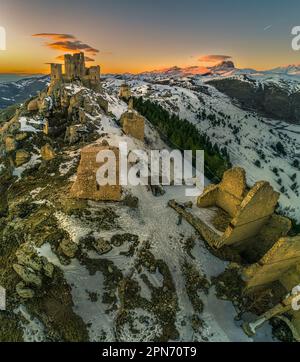 Veduta aerea della Rocca di Calascio con neve e illuminata dalla luce del tramonto, dietro la catena del Gran Sasso e del Corno grande. Foto Stock