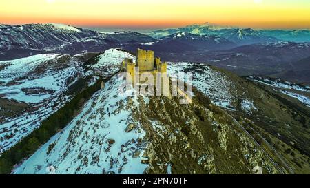 Veduta aerea della Rocca di Calascio con neve e illuminata dalla luce del tramonto, sullo sfondo le montagne del Parco Nazionale della Maiella. Foto Stock