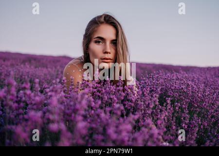 Campo di lavanda donna. Donna felice spensierata in vestito beige e cappello con grande orlo odore di una lavanda fiorente al tramonto. Perfetto per ispirare Foto Stock