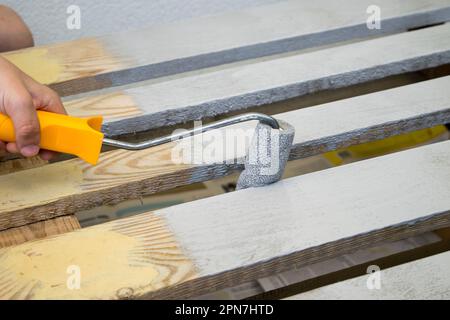 Verniciatura e colorazione con superficie in legno di colore bianco con rullo per pittura, primo piano Foto Stock