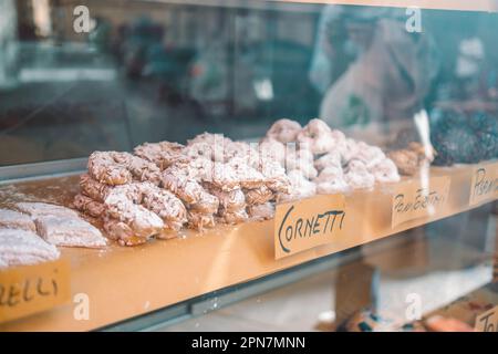 Cornetti italiani appena sfornati (cornetti) su un bancone in legno attraverso una vetrina. Foto di alta qualità Foto Stock