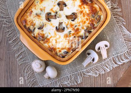 Torta di quiche fatta in casa con funghi (champignons) e formaggio su sfondo di legno, vista dall'alto. Torta di crostata saporita con funghi Foto Stock