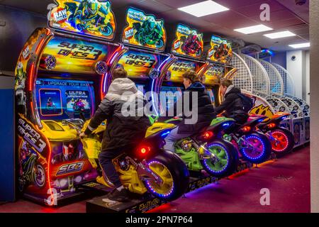 Amici adolescenti che giocano insieme su un gioco arcade di corse di moto in una galleria di divertimenti a Bournemouth, Regno Unito Foto Stock