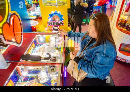 Una signora che si concentra, giocando una macchina delle cadute del penny in una galleria a Bournemouth, Regno Unito Foto Stock