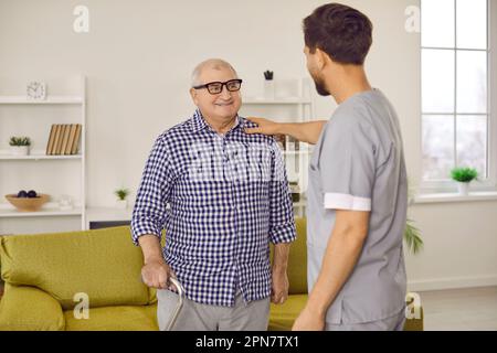 Giovane assistente maschile che sostiene il paziente anziano che tocca la spalla Foto Stock
