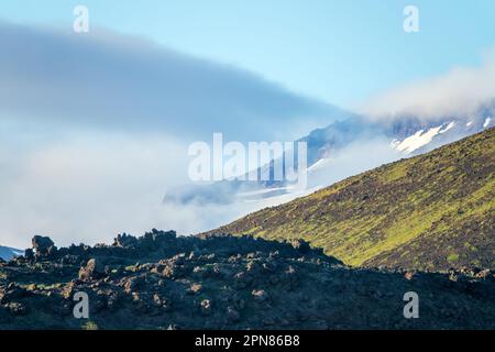Le nuvole rotolano nella valle. Panorama delle montagne vulcanogeniche. Lava e piroclasti in primo piano Foto Stock